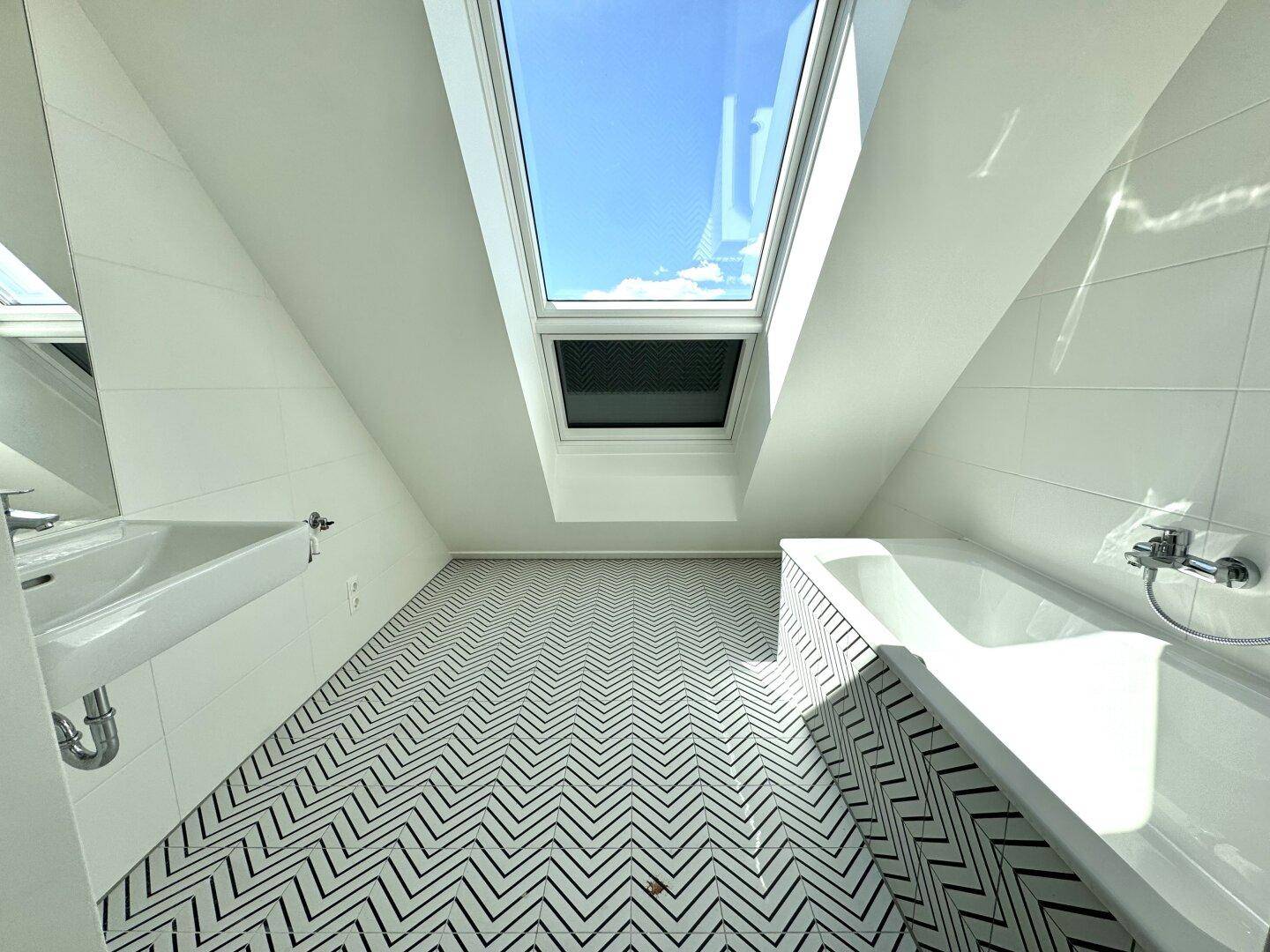 Modernes Badezimmer mit Badewanne, Waschbecken und großem Dachfenster, hell und stilvoll.