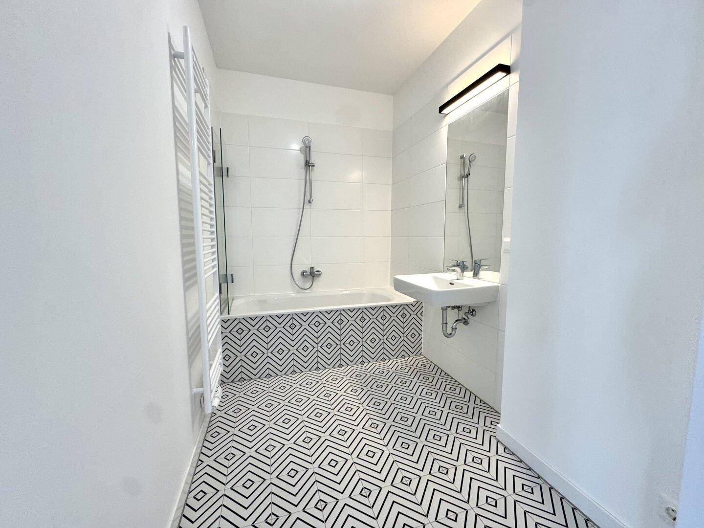 Modernes Badezimmer mit Badewanne, Duschfunktion, Waschbecken und geometrischen Bodenfliesen.