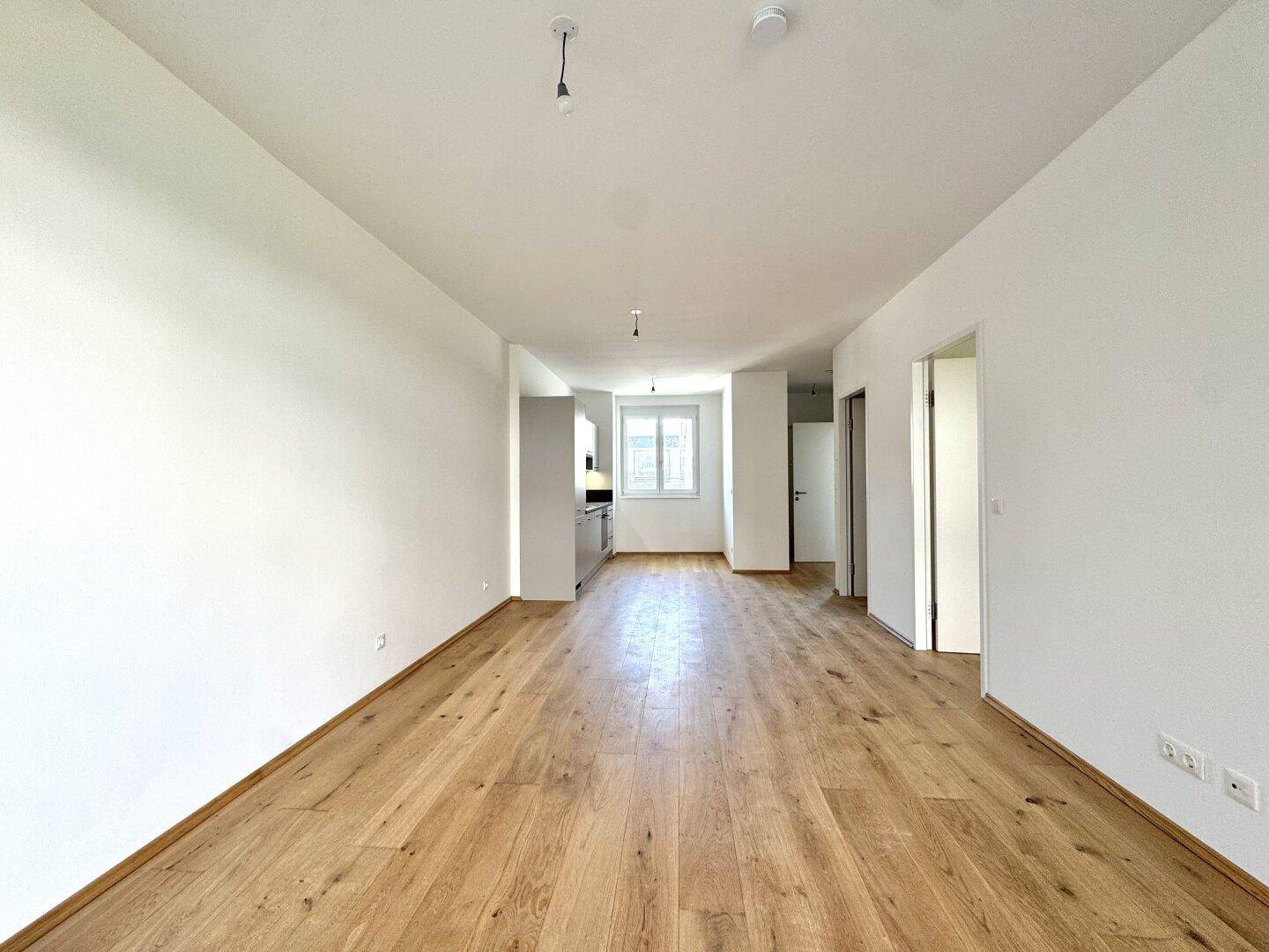 Geräumiger Wohn- und Essbereich mit hellem Holzboden und integrierter Küchenzeile.