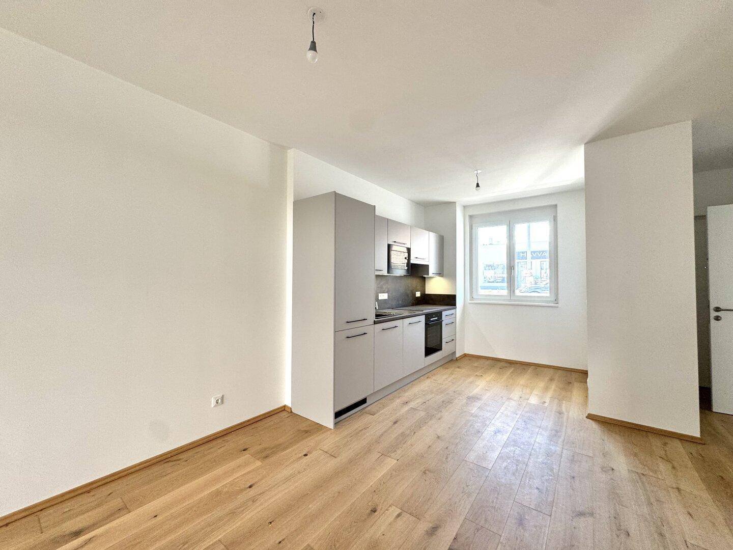 Moderne Küchenzeile mit grauen Schränken, Arbeitsplatte und Fenster in einem offenen Wohnbereich.