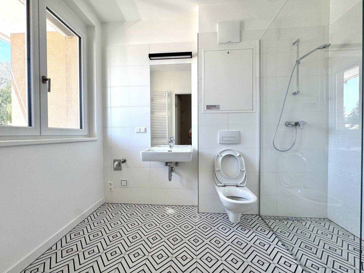 Modernes Badezimmer mit geometrischen Fliesen, begehbarer Dusche und Fenster für Tageslicht.