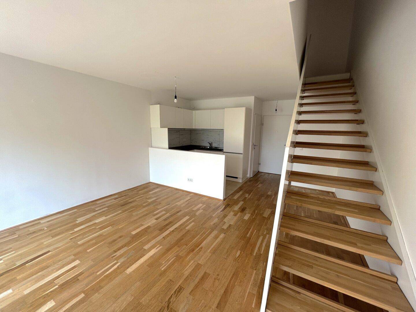 Offener Wohnbereich mit Holzboden, integrierter Küchenzeile und Holztreppe, hell und modern gestaltet.
