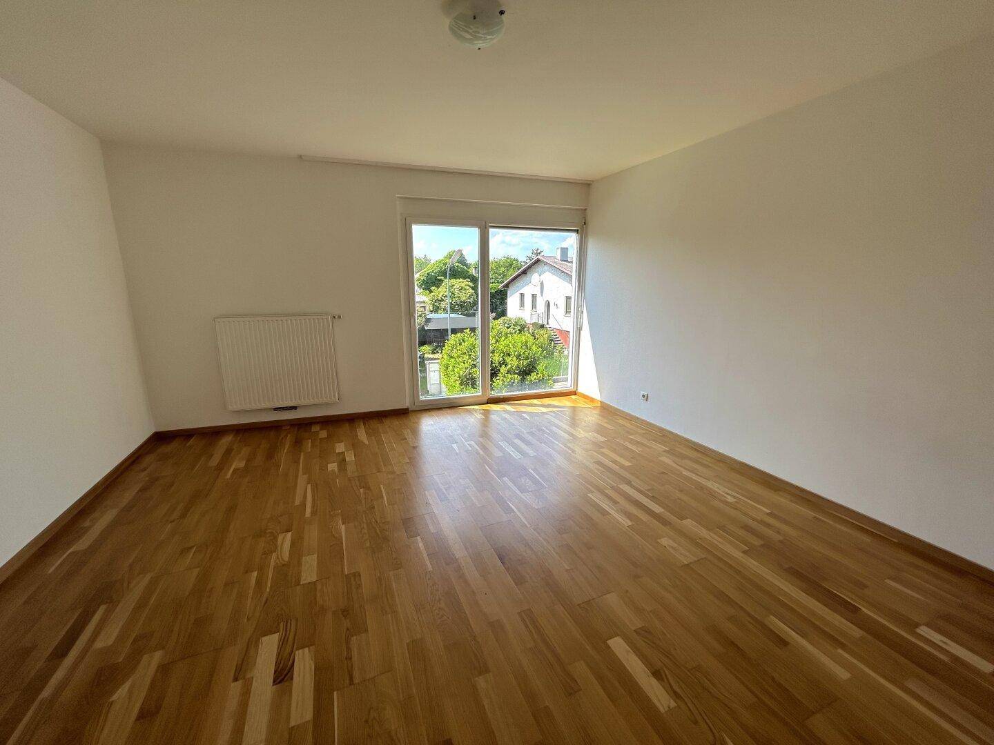 Geräumiges Zimmer mit Holzboden und großer Fensterfront, die viel Tageslicht hereinlässt.