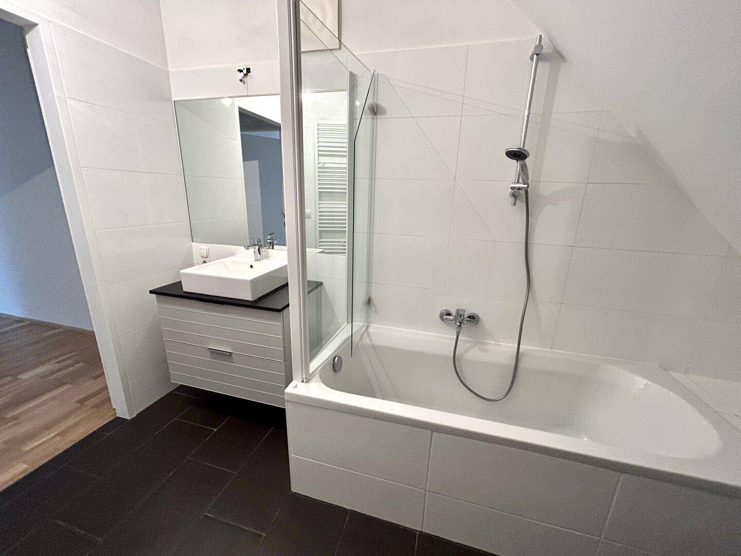 Modernes Badezimmer mit Badewanne, Duschvorrichtung, Einzelwaschbecken und Handtuchheizkörper.