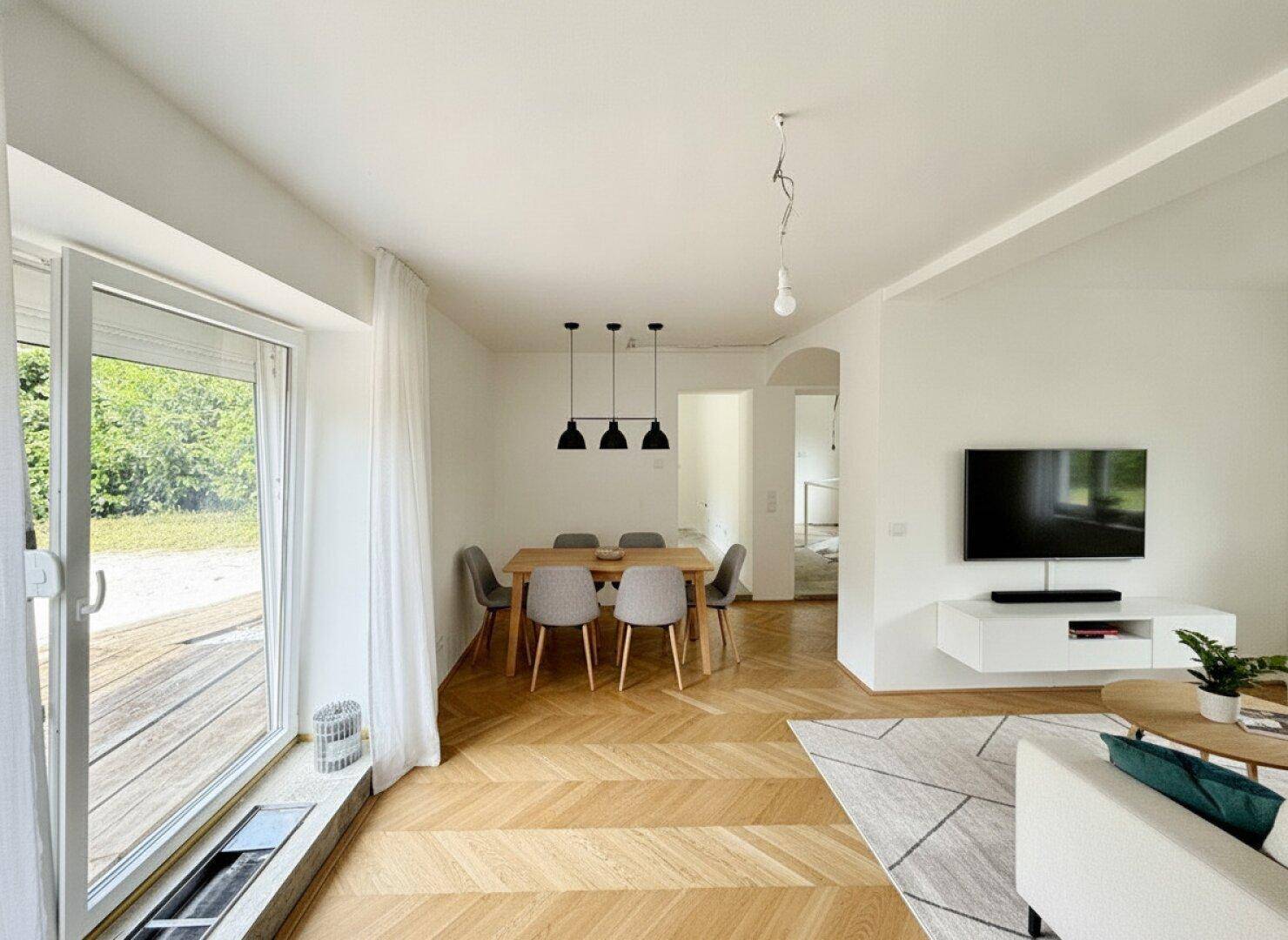 Moderner Wohn-Essbereich mit Fischgrätparkett, stilvoller Einrichtung und Zugang zur Terrasse.