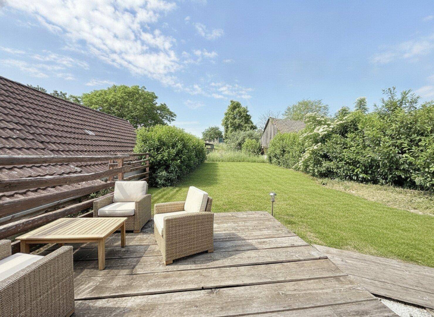 Gemütliche Holzterrasse mit Gartenmöbeln und Blick auf den weitläufigen grünen Garten.