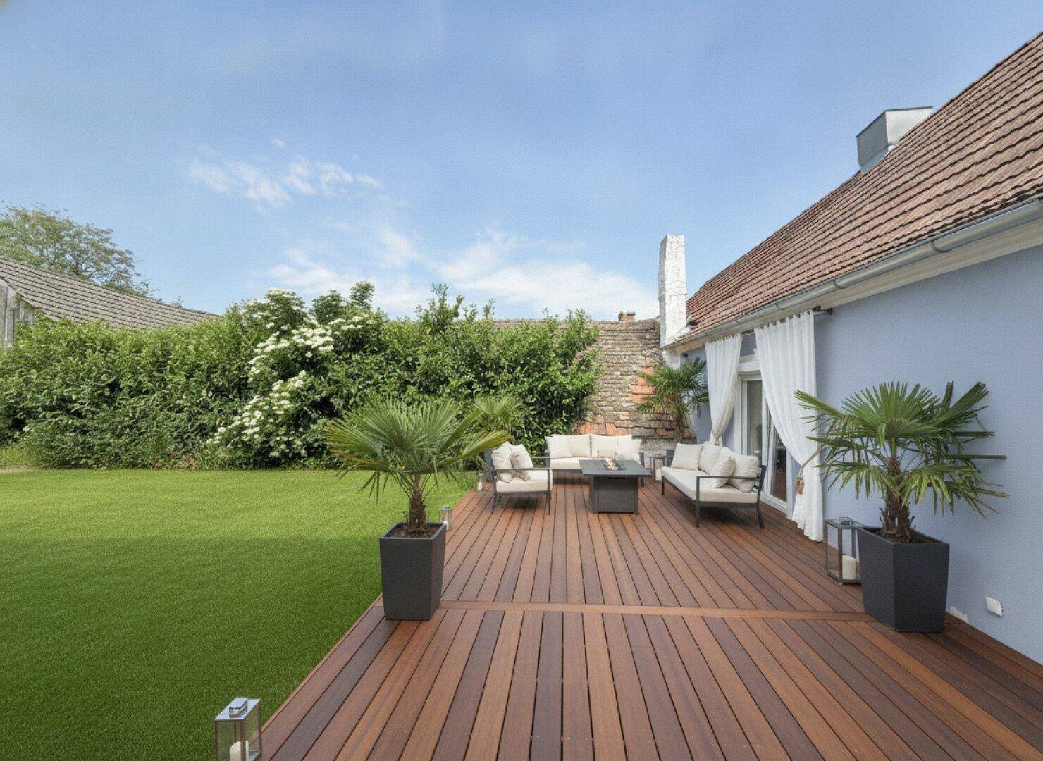 Große Holzterrasse mit bequemen Lounge-Möbeln, Palmen und Blick auf den grünen Garten.