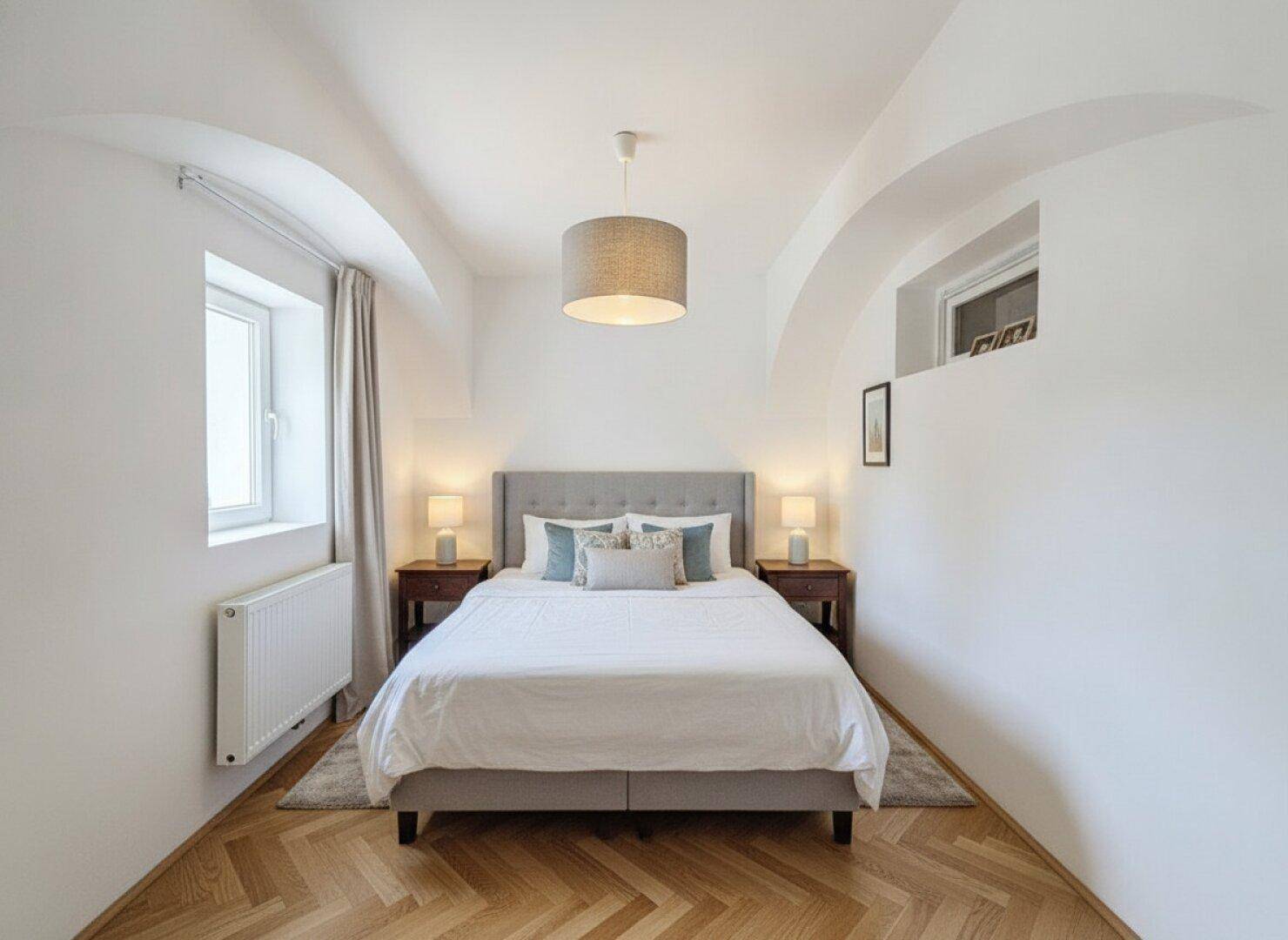 Gemütliches Schlafzimmer mit Doppelbett, Nachttischen, Lampen und Fischgrätparkettboden.
