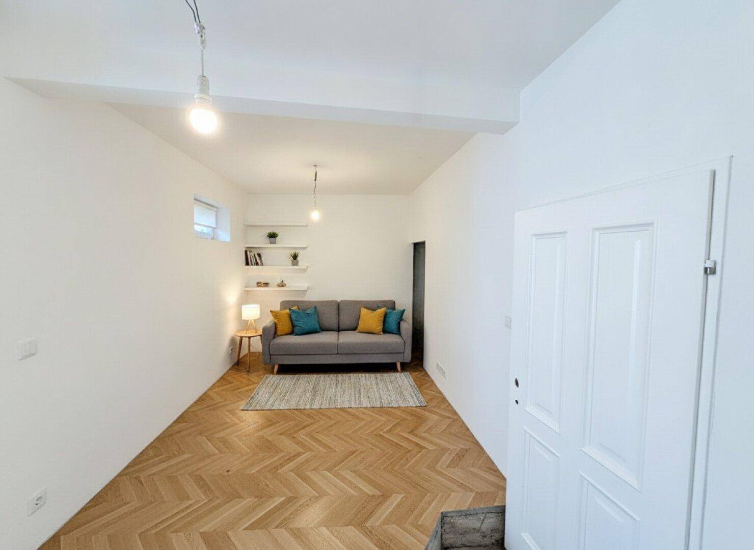 Gemütliches Wohnzimmer mit Sofa, Teppich, Regalen und elegantem Fischgrätparkettboden.