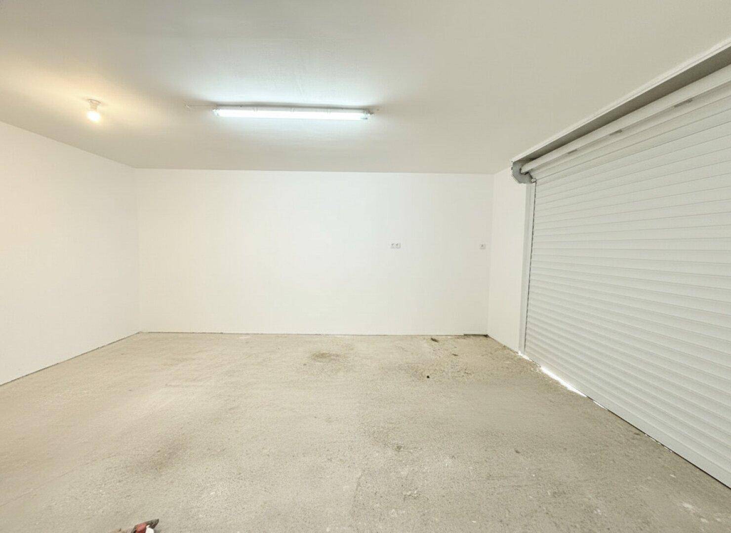 Leere Garage mit Rolltor und Betonboden, bereit für die Nutzung als Stellplatz.