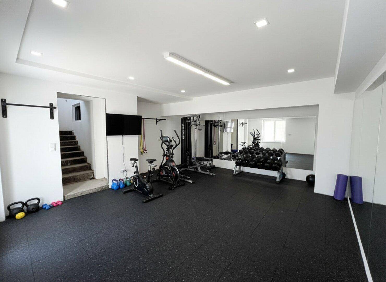 Moderner Fitnessraum mit Sportgeräten, Hanteln und Spiegelwänden, ideal für Training.