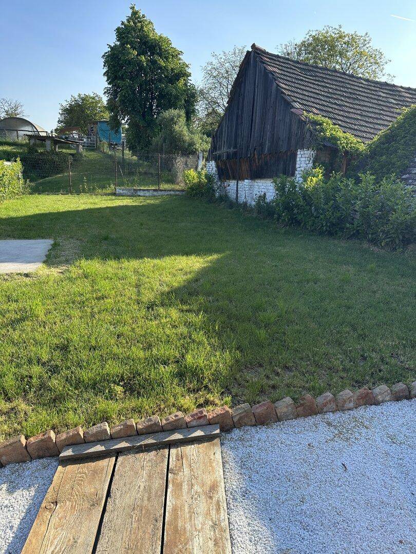 Weitläufiger Garten mit Rasenfläche und ländlicher Umgebung unter strahlend blauem Himmel.