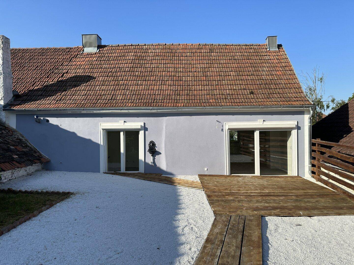 Geräumige Terrasse mit Holzdeck und Kiesfläche, angrenzend an ein renoviertes Landhaus.