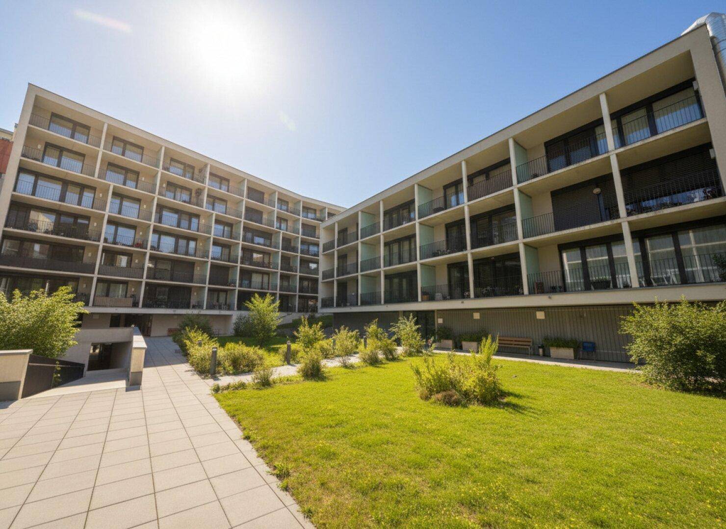 Moderner Apartmentkomplex mit Innenhof und Grünflächen unter blauem Himmel.