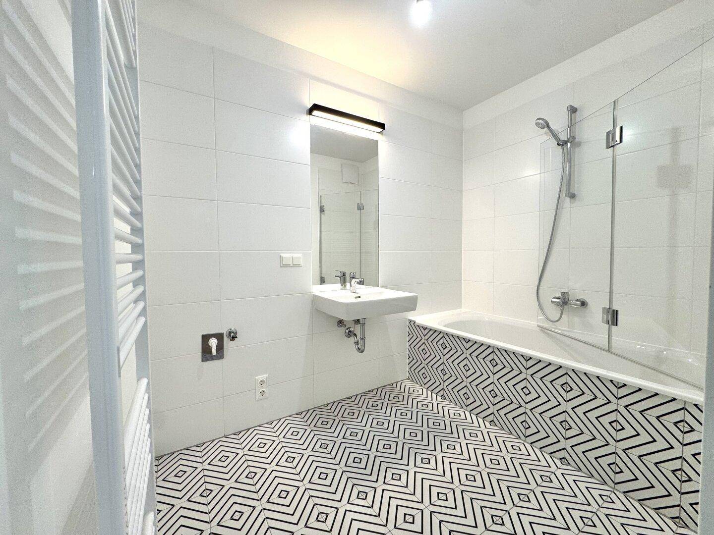 Modernes Badezimmer mit Badewanne, Duschabtrennung und auffälligem geometrischem Fliesenboden.