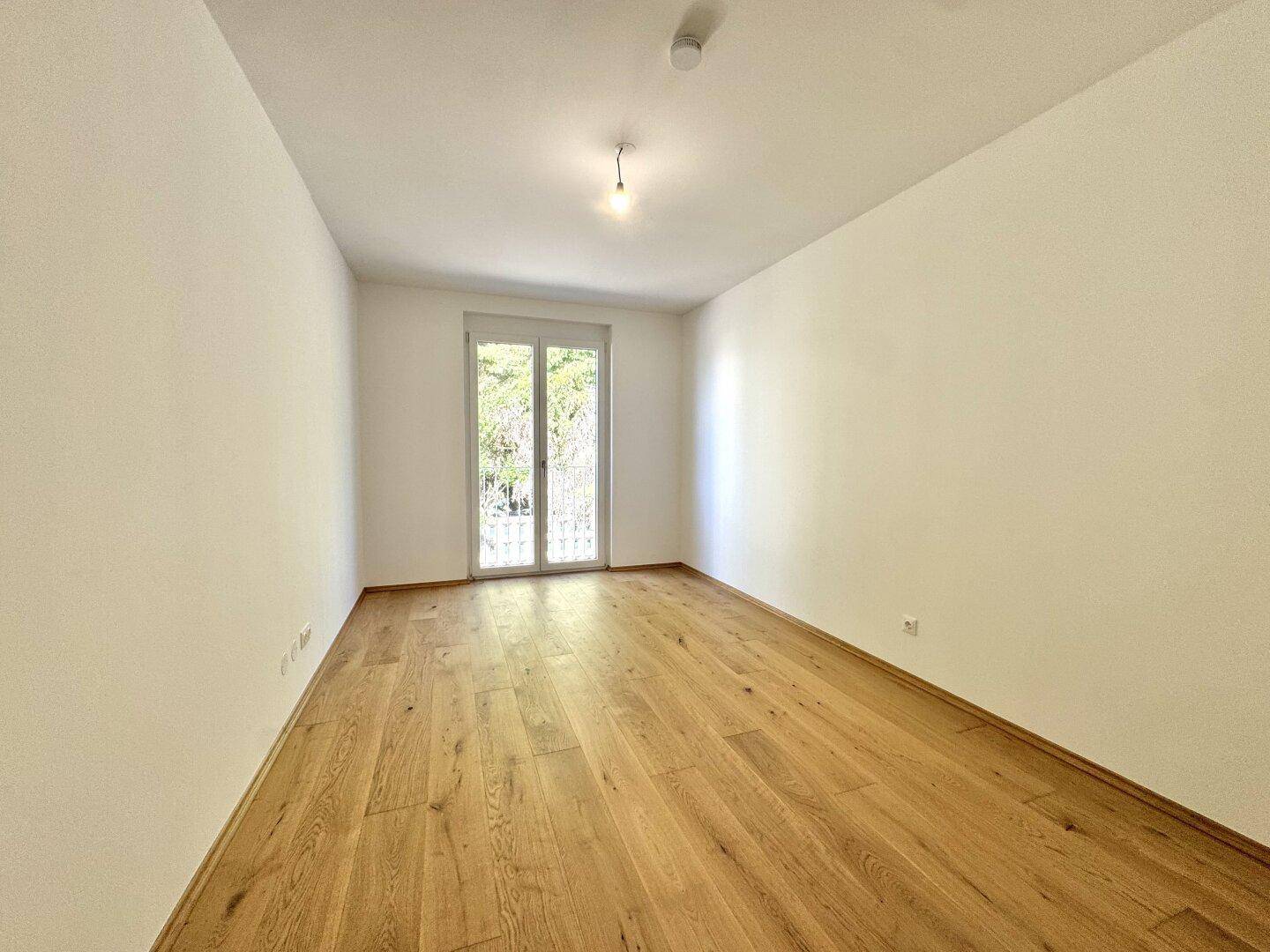 Helles Zimmer mit Holzboden und Zugang zu einem französischen Balkon, ideal als Schlafzimmer.