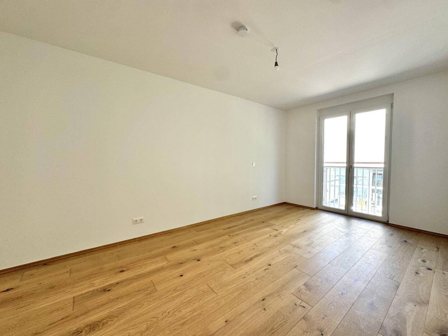 Geräumiges Zimmer mit Holzboden und Balkonzugang, vielseitig nutzbar als Schlaf- oder Arbeitszimmer.