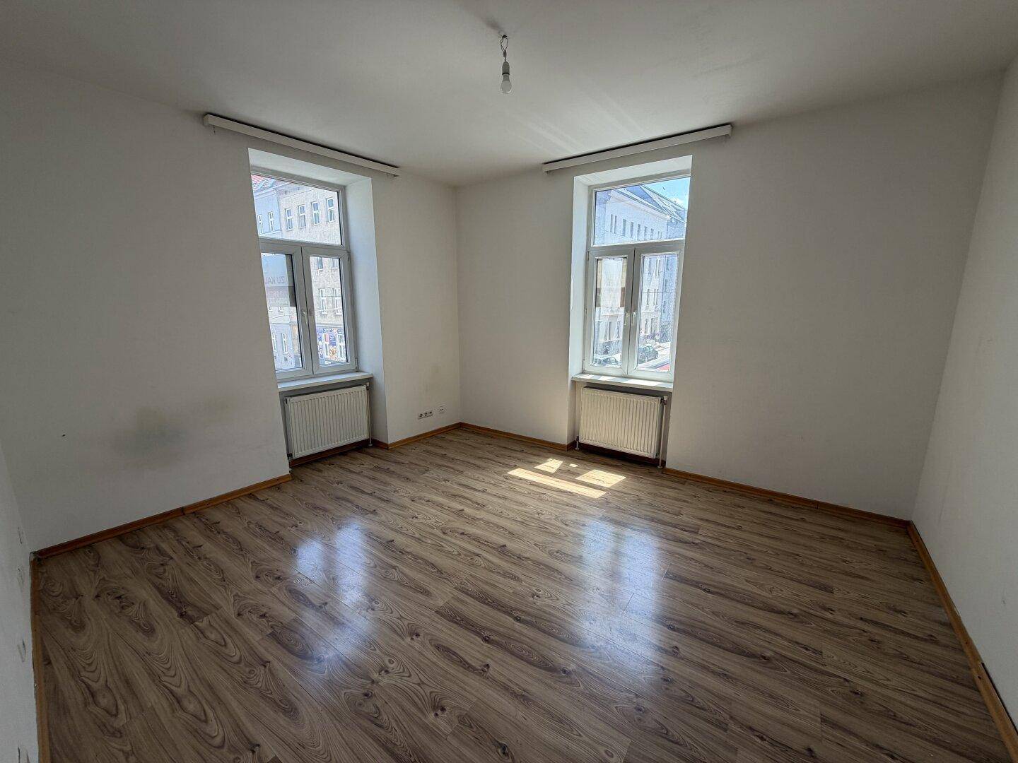 Heller, leerer Raum mit Laminatboden und zwei Fenstern, bereit zur individuellen Gestaltung.