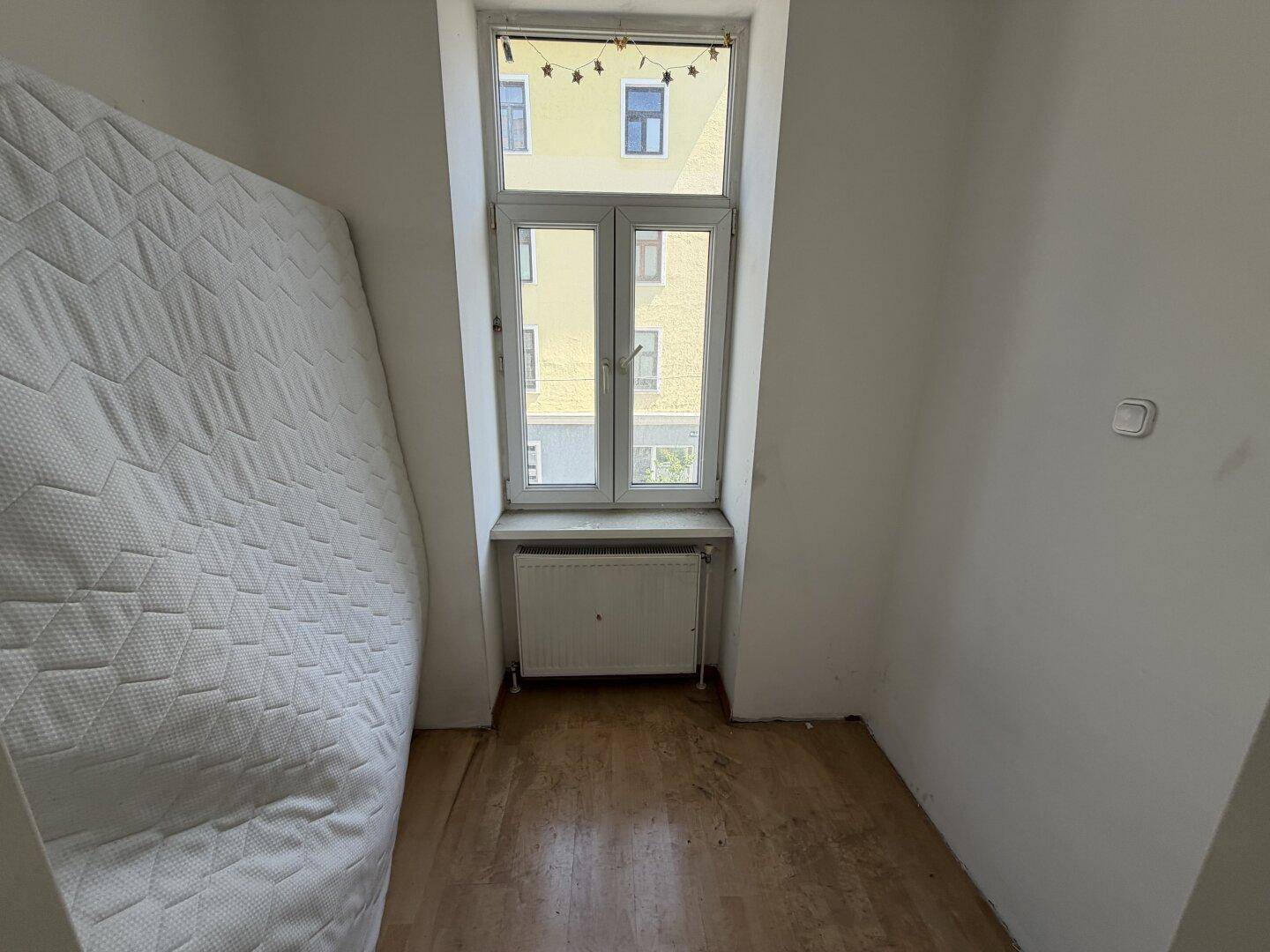 Kleines Schlafzimmer mit einem Fenster und einfacher Ausstattung, ideal für eine Einzelperson.