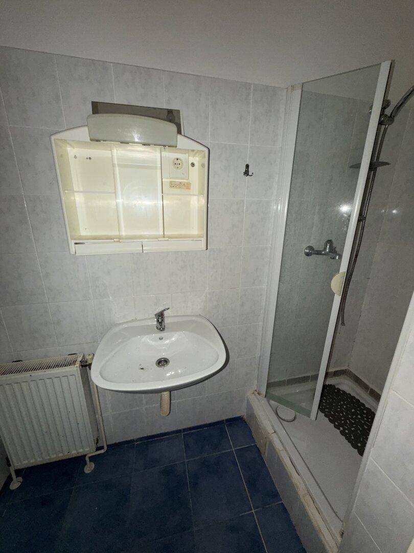 Funktionales Badezimmer mit Duschkabine, Waschbecken und blauen Bodenfliesen.
