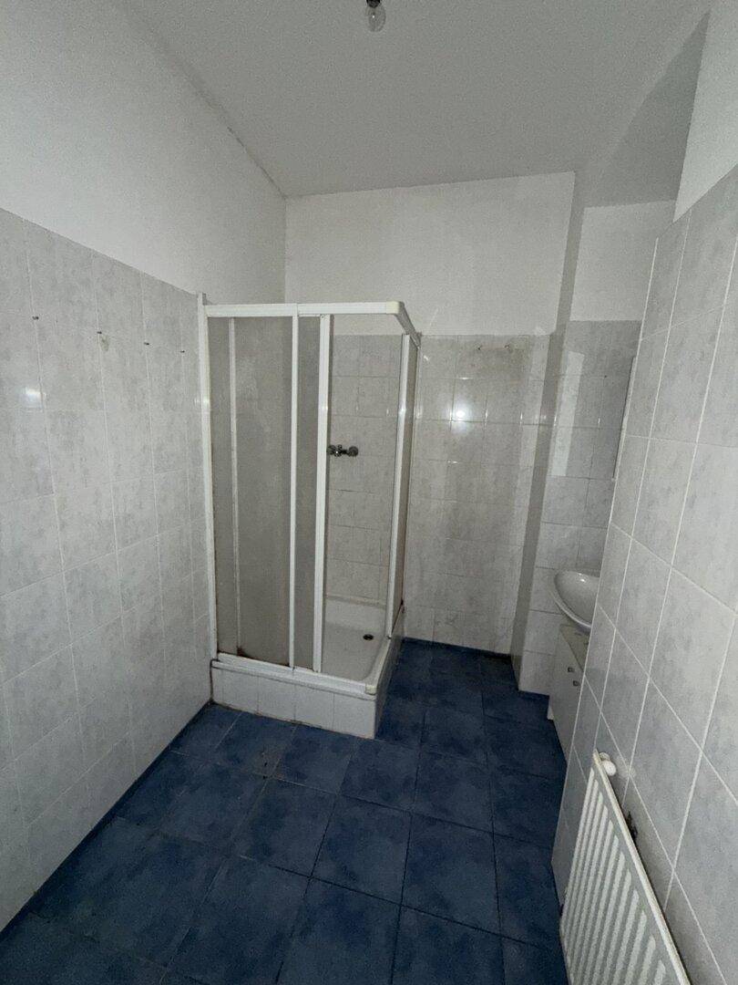Badezimmer mit blauen Bodenfliesen, weißer Duschkabine und Wandfliesen.