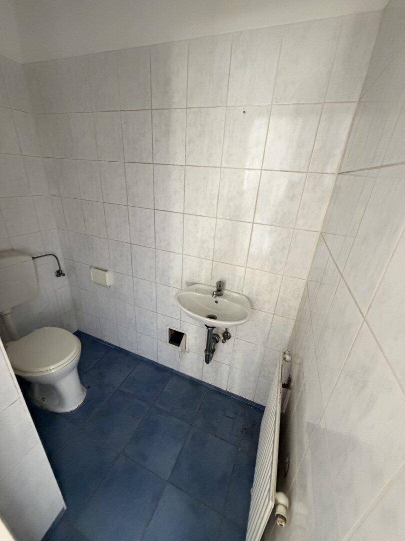 Kleines WC mit Toilette, Waschbecken und blauen Bodenfliesen.
