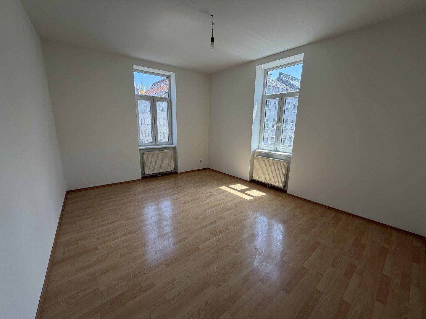 Geräumiger, unmöblierter Raum mit Laminatboden und viel Tageslicht durch zwei Fenster.