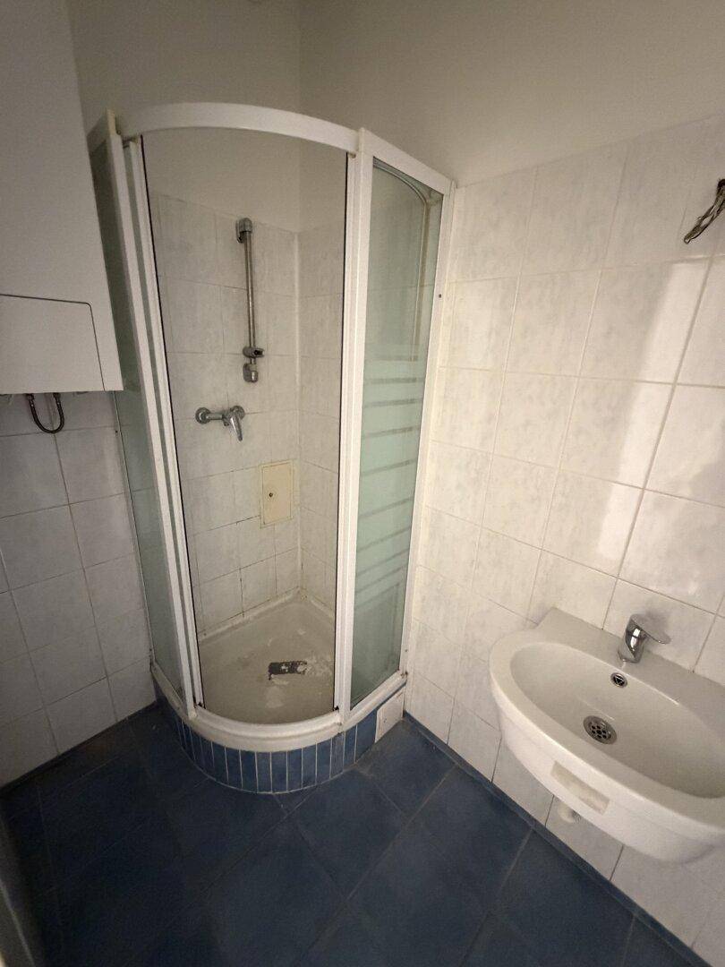 Badezimmer mit Eckduschkabine, Waschbecken, weißen Wandfliesen und dunkelblauem Boden.