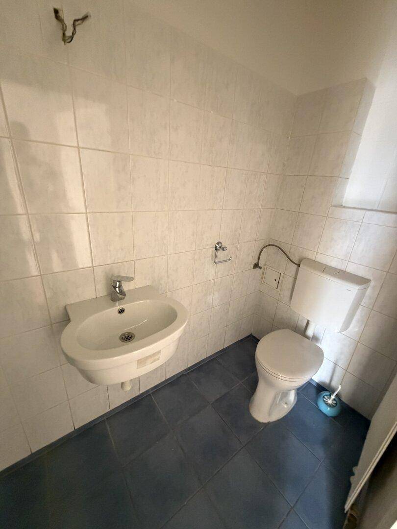 Separates WC mit Toilette, Waschbecken, weißen Fliesen und einem kleinen Fenster.