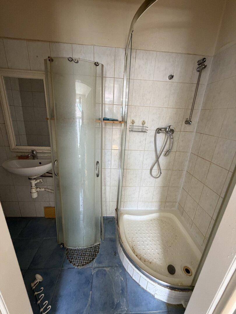 Badezimmer mit Duschkabine, Waschbecken und blauen Bodenfliesen in älterem Zustand.