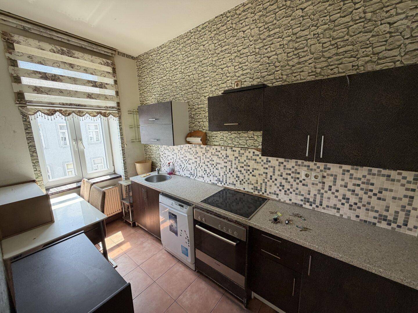 Küche mit dunklen Schränken, Fliesenboden und einem Fenster mit Jalousie.