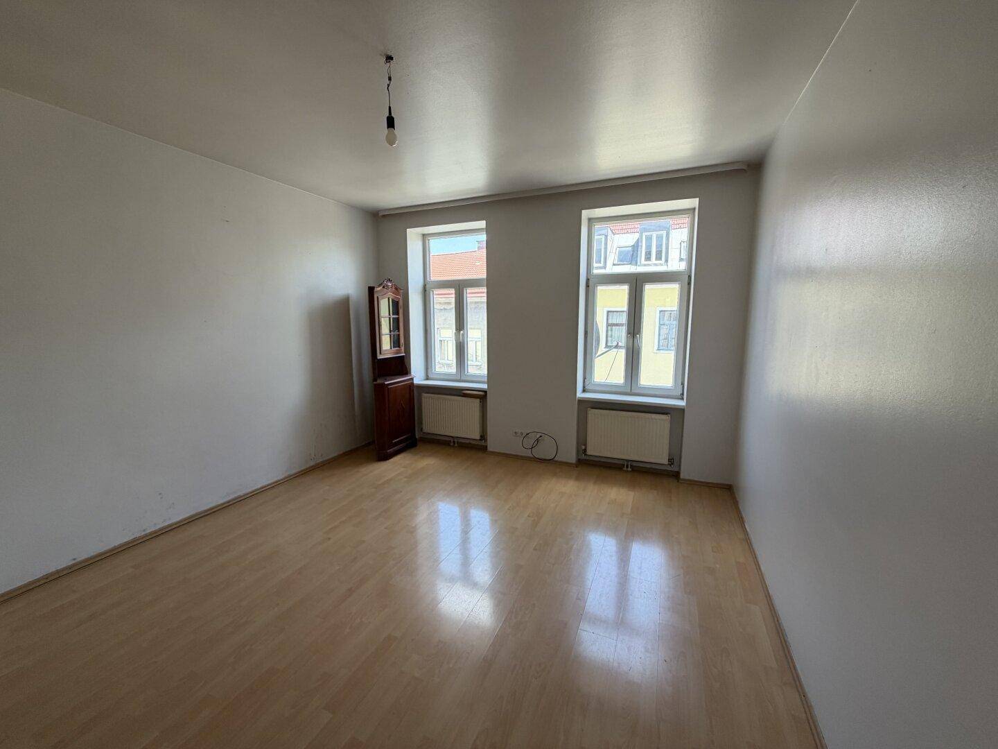Heller, leerer Wohnraum mit Laminatboden und zwei Fenstern, bereit zur individuellen Gestaltung.