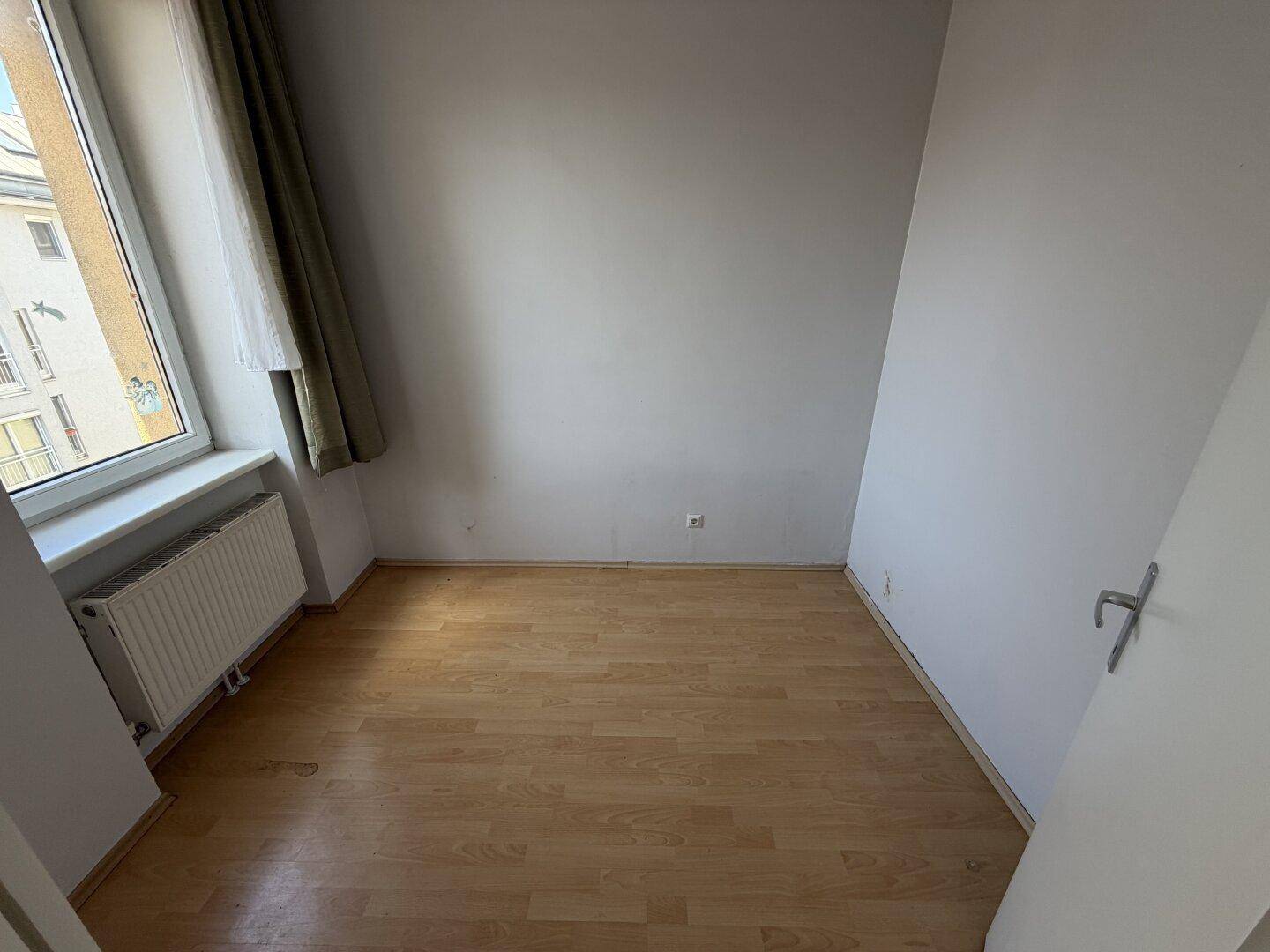 Kleines, helles Zimmer mit Laminatboden und Fenster, ideal als Schlafzimmer oder Arbeitsbereich.
