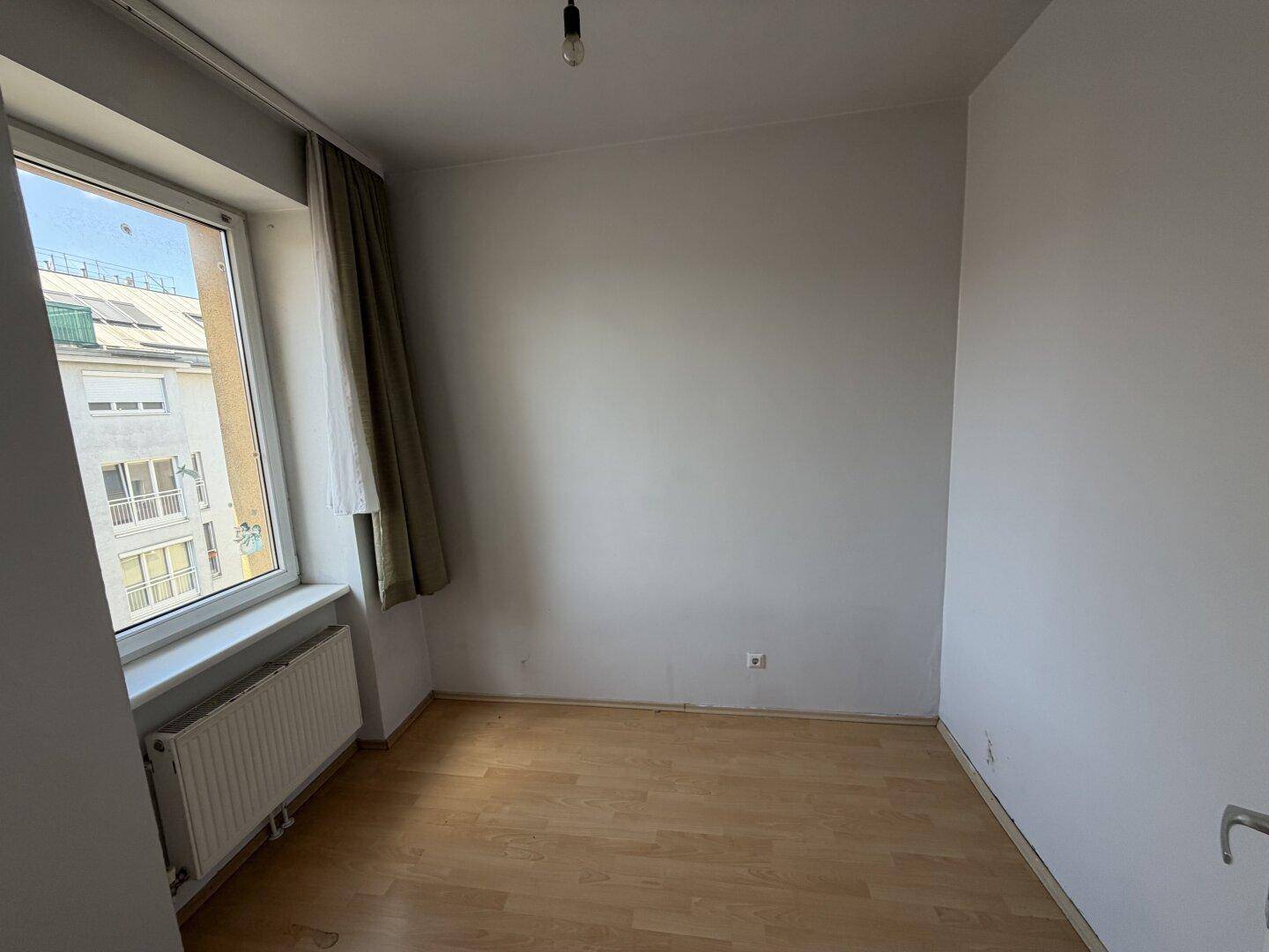 Lichtdurchflutetes Zimmer mit Laminatboden und Blick auf die umliegenden Gebäude.