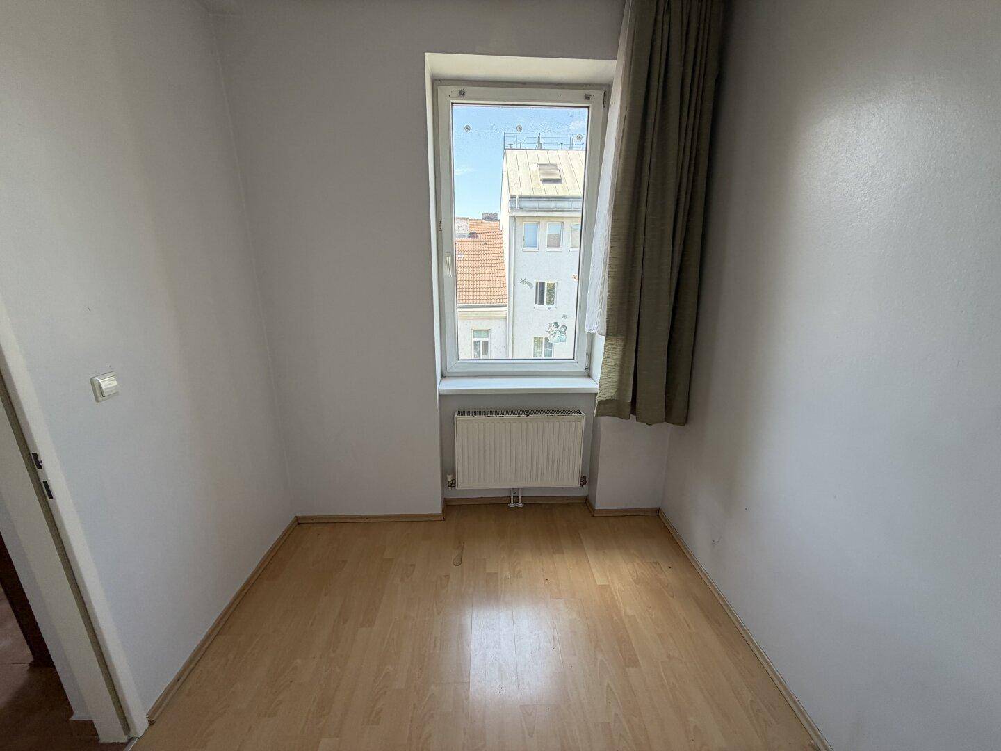 Schmales, helles Zimmer mit Laminatboden und einem hohen Fenster, vielseitig nutzbar.