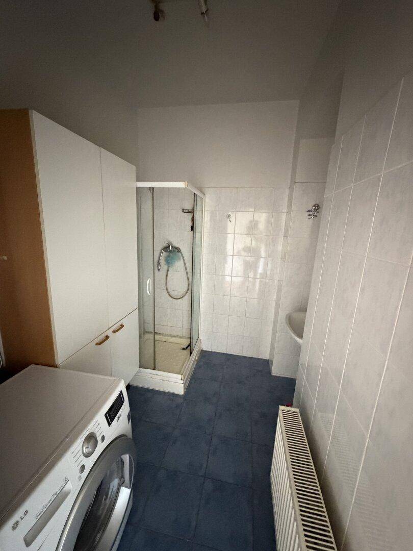 Funktionales Badezimmer mit Duschkabine, Waschmaschinenanschluss und weißen Wandfliesen.