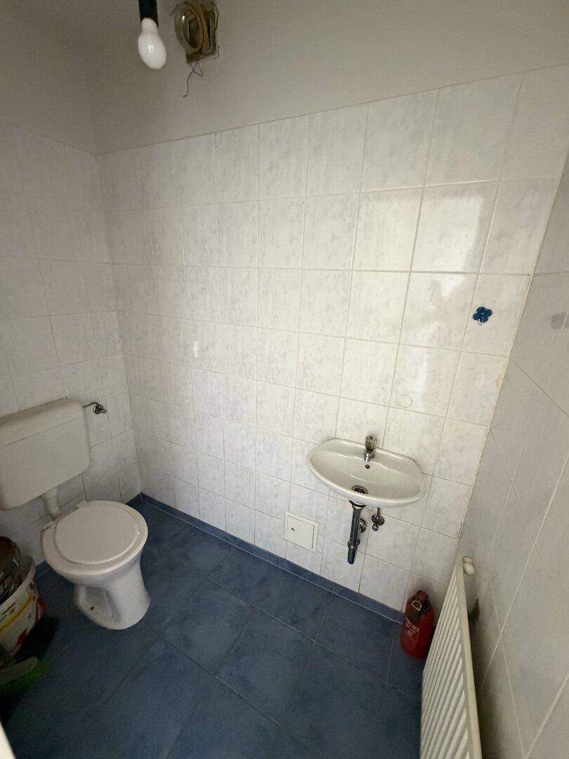 Separate Gästetoilette mit WC, kleinem Waschbecken und blauen Bodenfliesen.