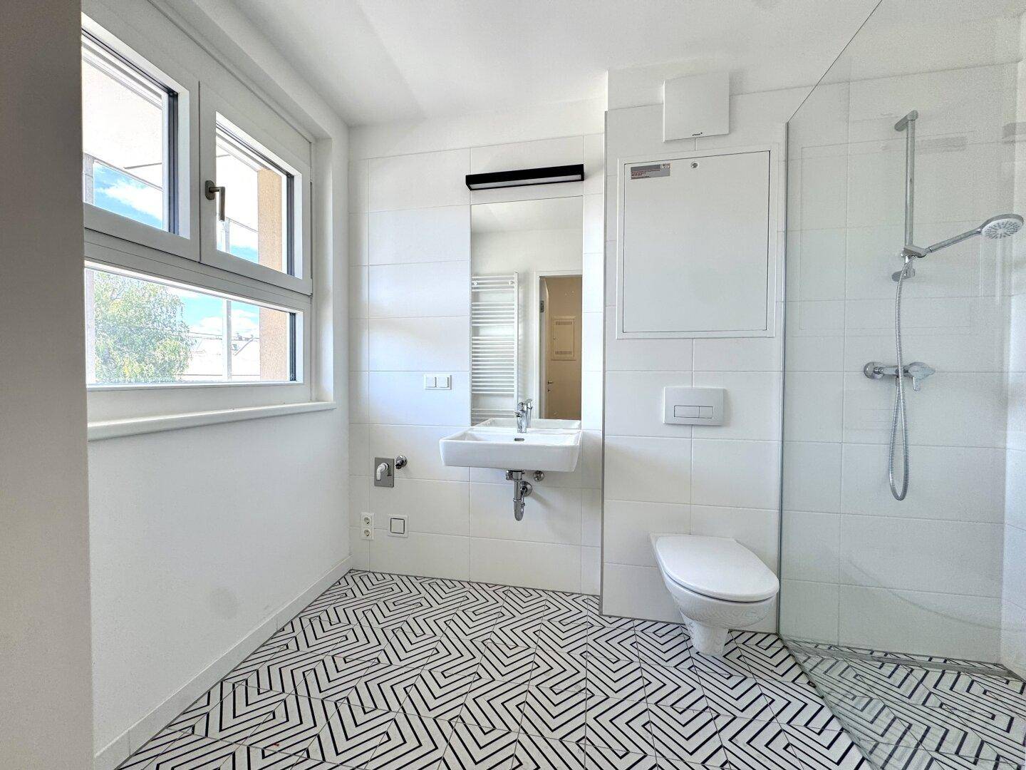 Modernes Badezimmer mit Fenster, begehbarer Dusche, Einzelwaschbecken und gemusterten Fliesen.
