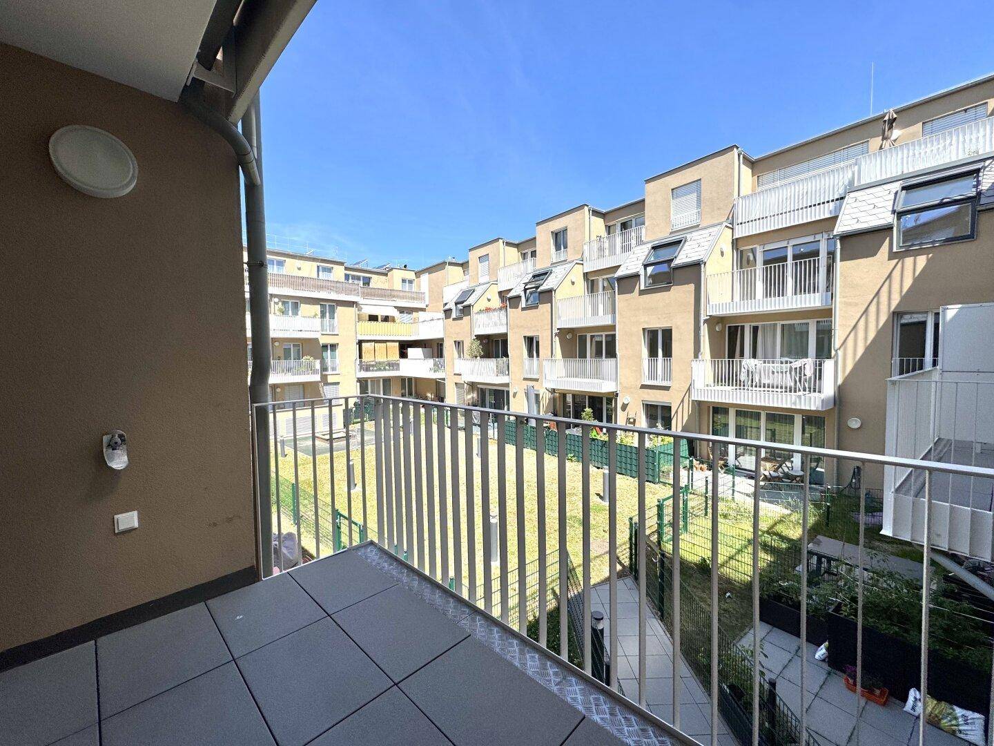 Balkon mit Blick auf den begrünten Innenhof und die umliegenden Wohngebäude.