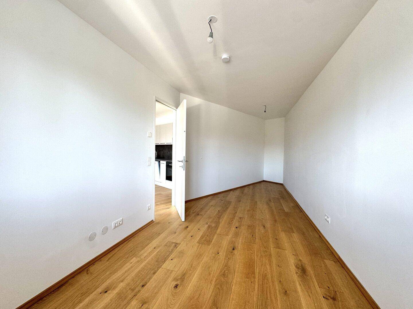 Leerer Raum mit Holzboden und weiß gestrichenen Wänden, bereit zur individuellen Gestaltung.