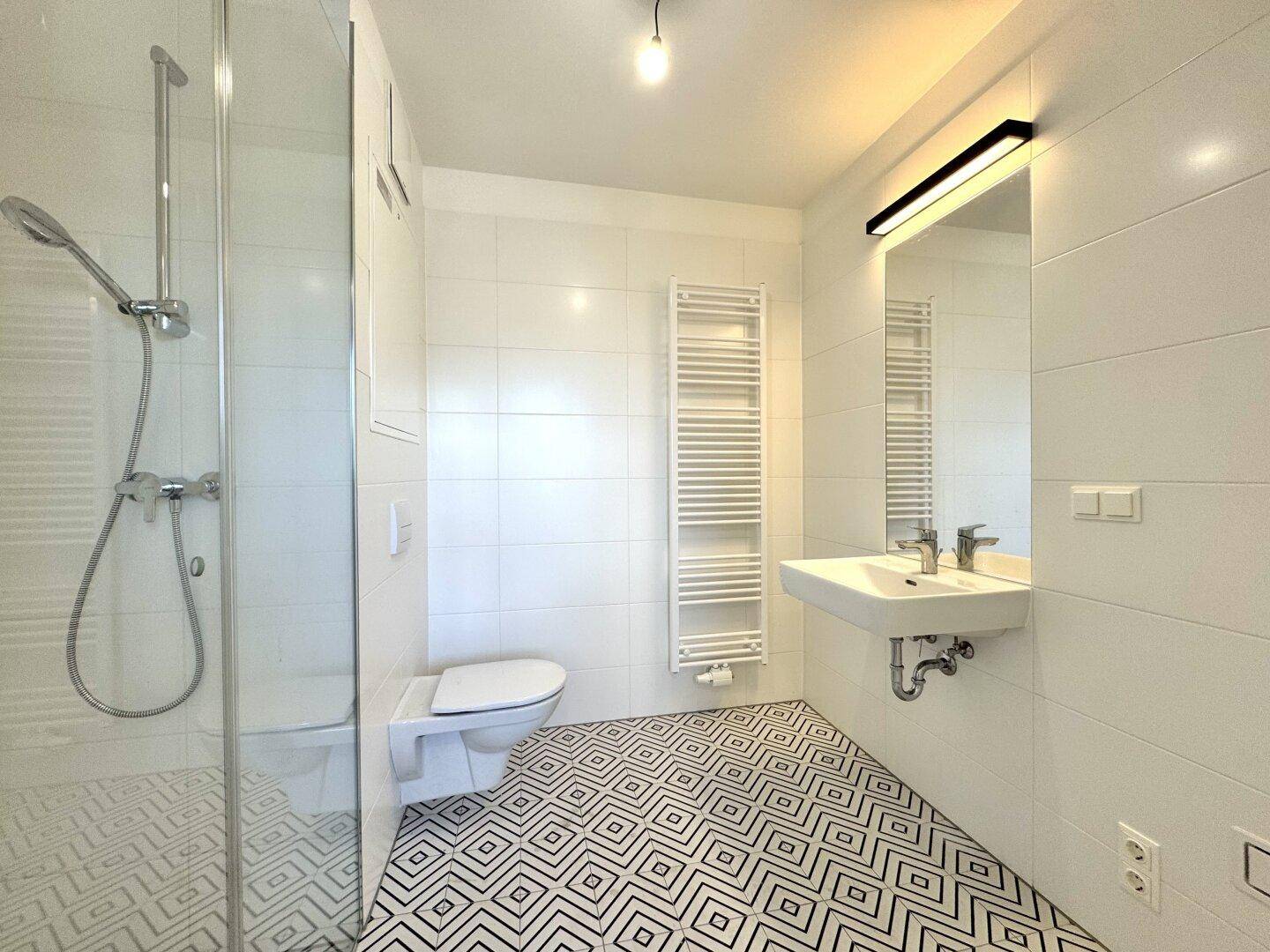 Modernes Badezimmer mit Duschkabine, Wand-WC, Waschbecken und gemusterten Fliesen.