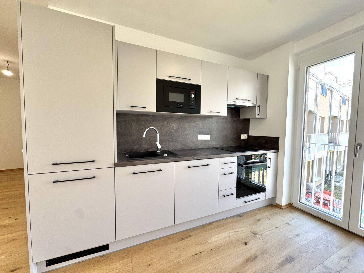 Moderne Einbauküche mit grauen Fronten, integrierten Geräten und direktem Zugang zum Balkon.