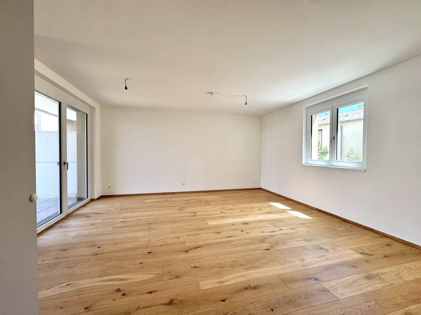 Helles Zimmer mit Eichenparkett, großen Fenstern und Zugang zu einem Außenbereich.