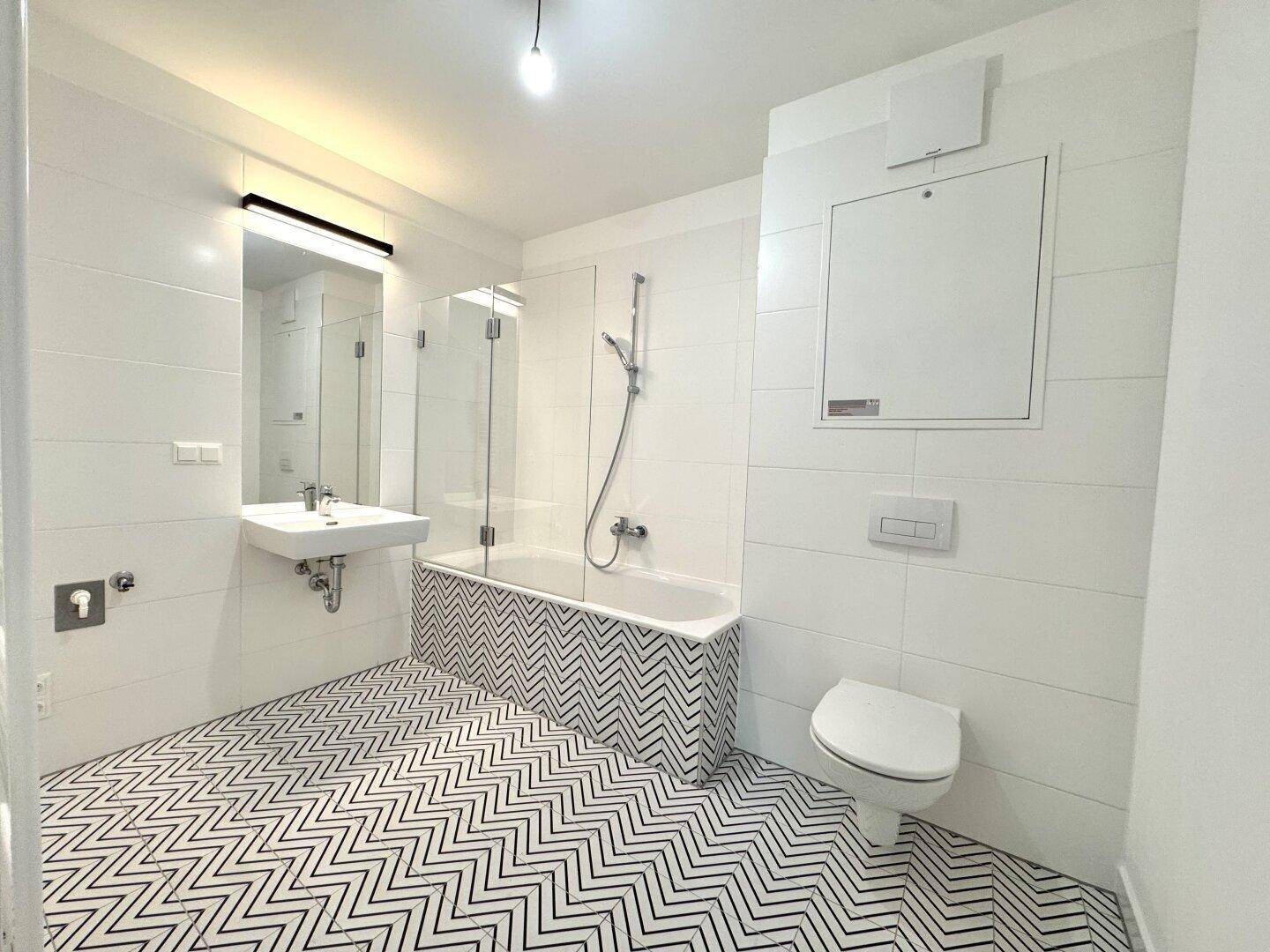 Modernes Badezimmer mit weißen Fliesen, Badewanne, Einzelwaschbecken und Wand-WC.