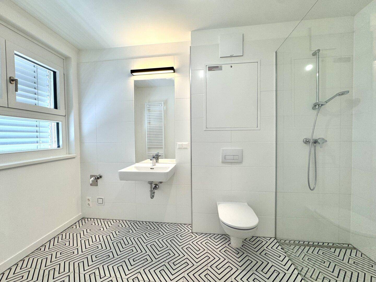 Modernes Badezimmer mit geometrischen Fliesen, ebenerdiger Dusche, Fenster und Handtuchheizkörper.