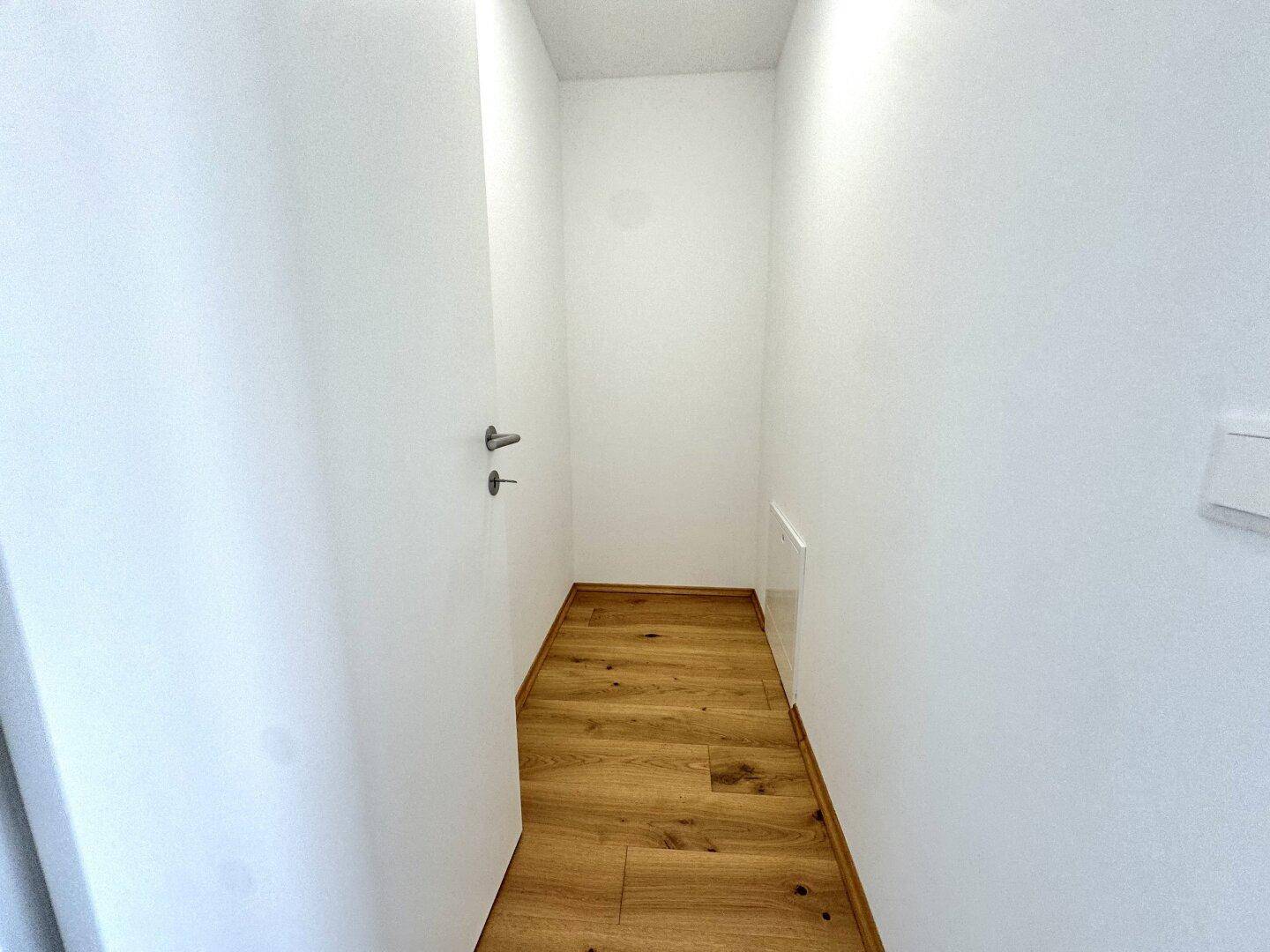 Heller Flur mit Holzboden und weiß gestrichenen Wänden, der zu weiteren Räumen führt.