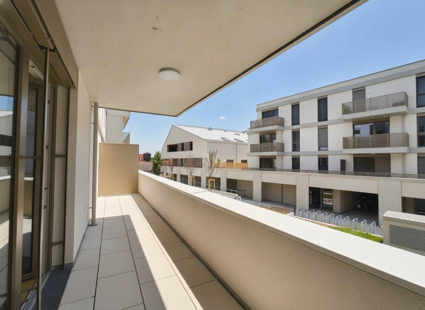 Langer Balkon mit Fliesenboden und Aussicht auf die moderne Wohnanlage.