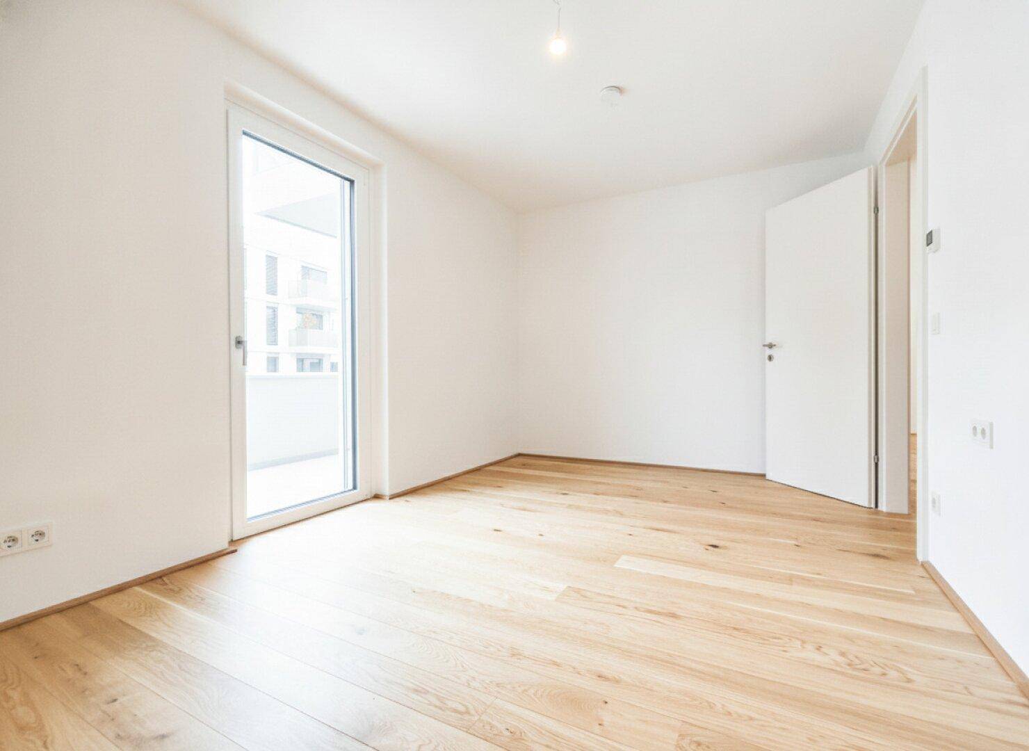 Helles Zimmer mit Holzboden und Zugang zu einem Balkon, ideal als Schlaf- oder Arbeitszimmer.
