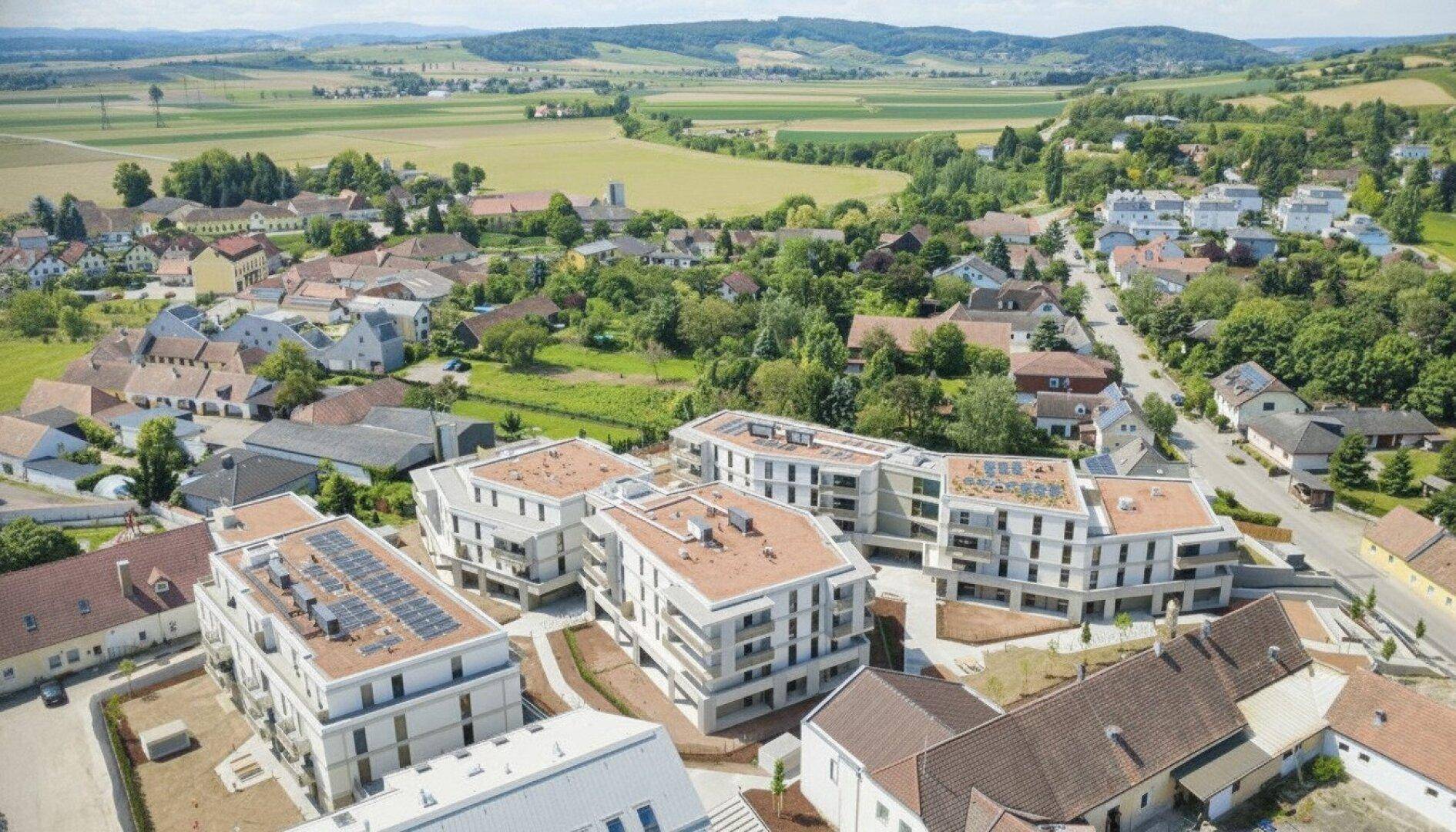 Luftaufnahme der neuen Wohnsiedlung umgeben von grünen Hügeln und ländlicher Landschaft.