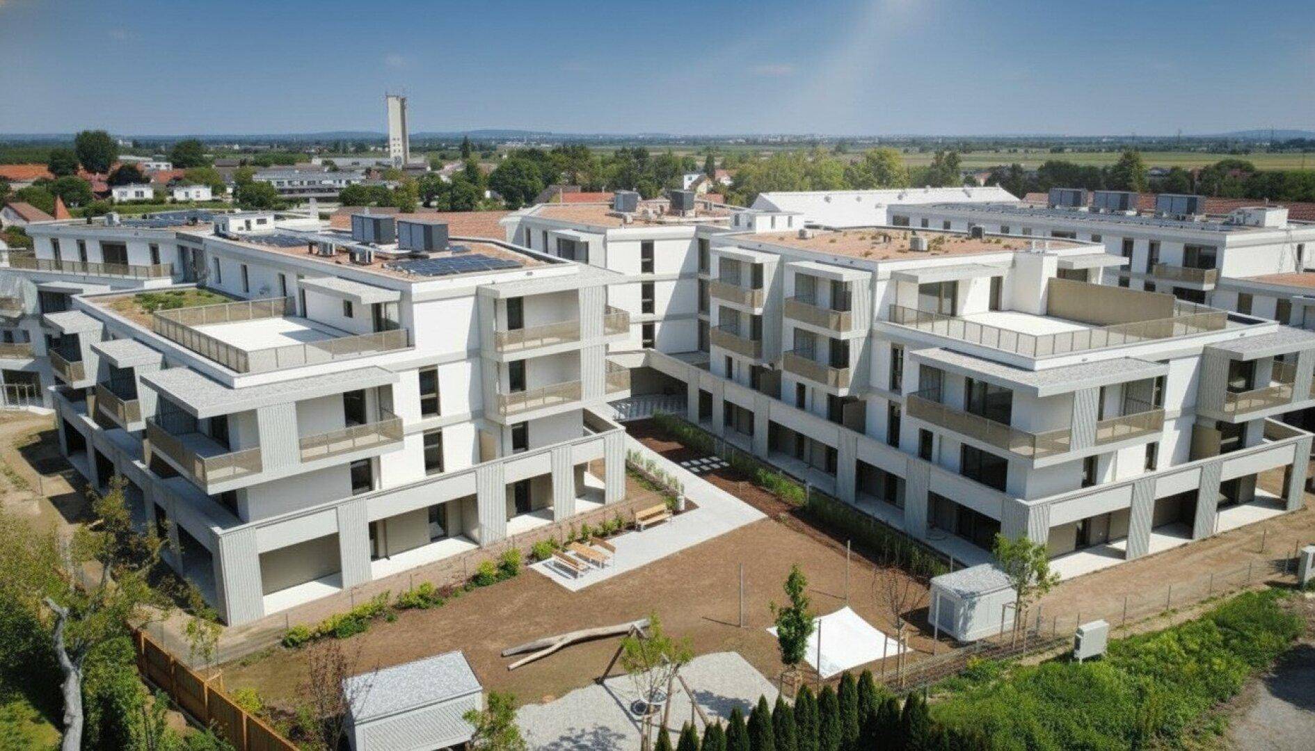 Luftaufnahme der Wohnanlage mit Spielplatz und Gemeinschaftsflächen, umgeben von Natur.